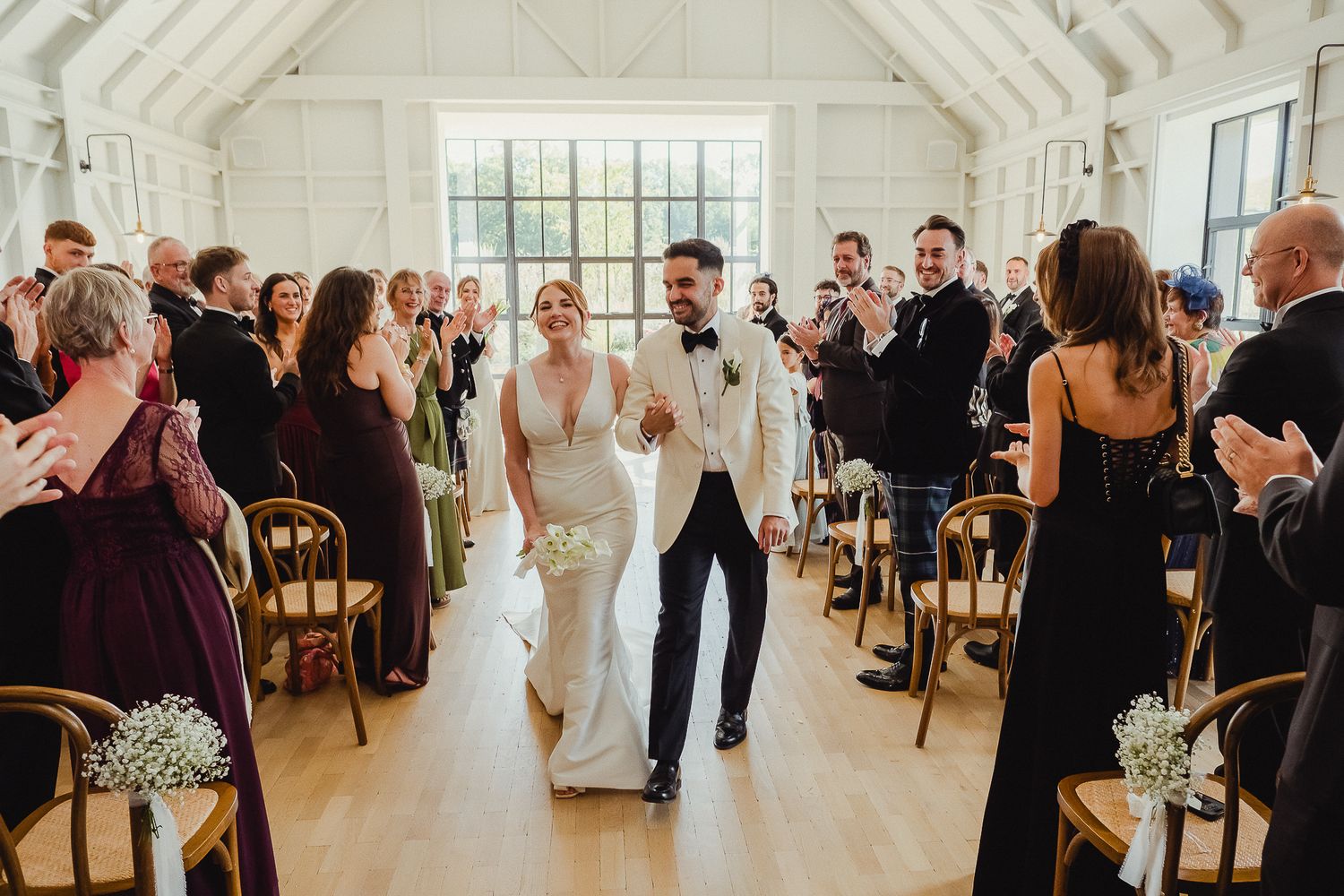 Wedding guests dance and celebrate during a joyful reception in a bright indoor venue.