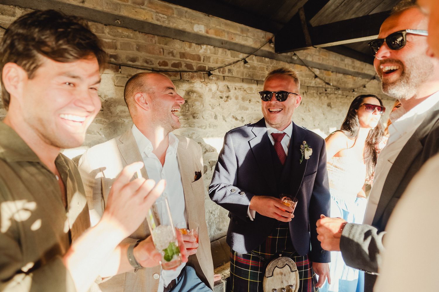 Wedding guests laugh and socialize during an outdoor celebration at a rustic venue.