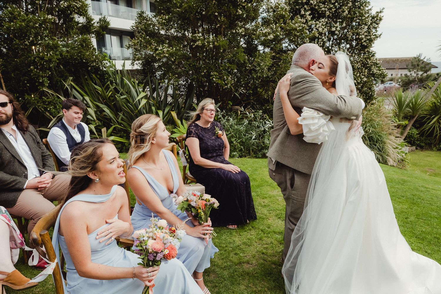 Wedding party members celebrate on a sunny lawn with joyful expressions and gestures.