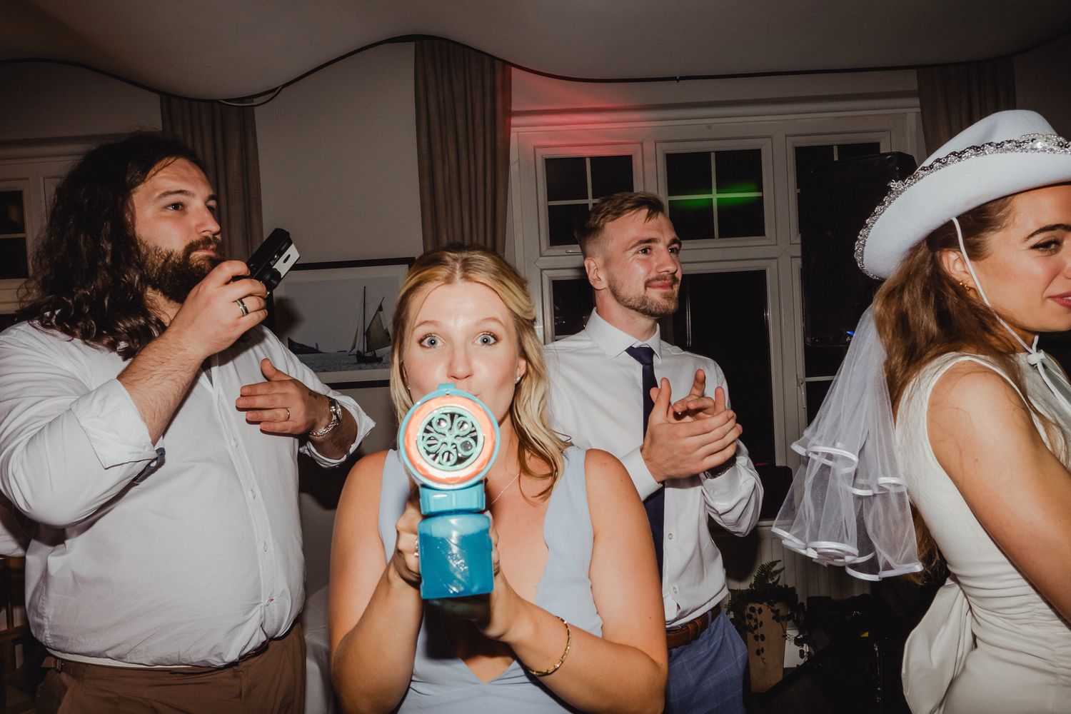 People dancing and celebrating at a wedding party with drinks and laughter in an indoor venue.