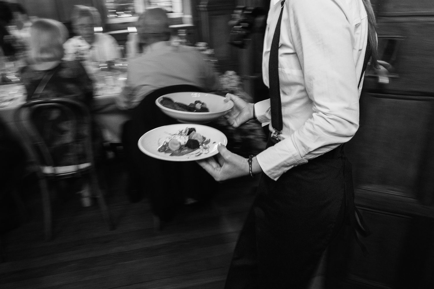 Waiter carrying two plates of food in a busy restaurant, black and white photo.