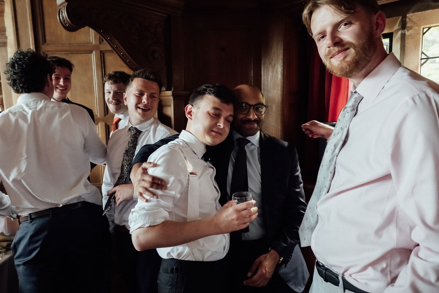 Group of young men in dress shirts laughing and socializing at a wedding reception.