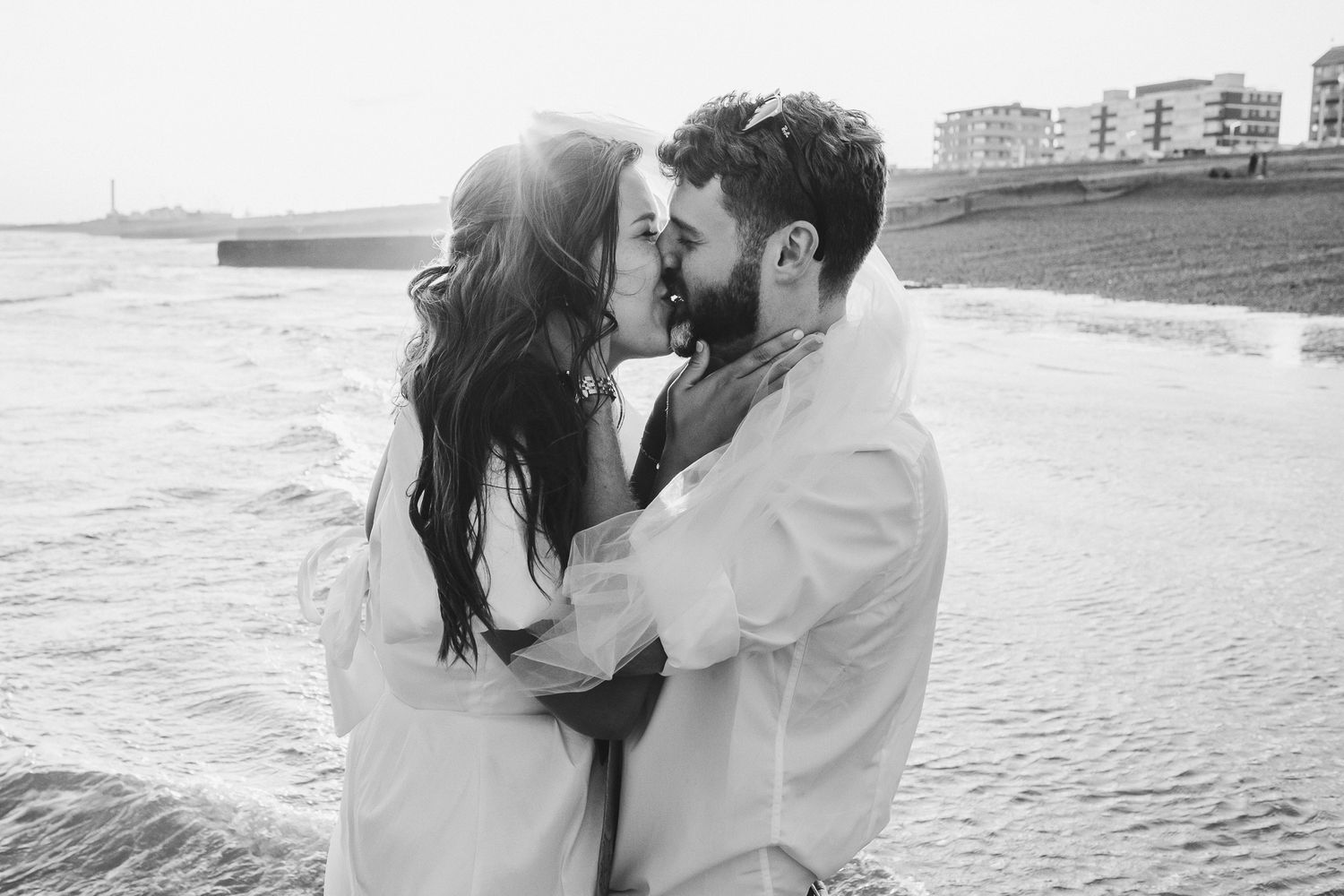 Black and white photo of a couple sharing a romantic moment and embracing at the beach during sunset.
