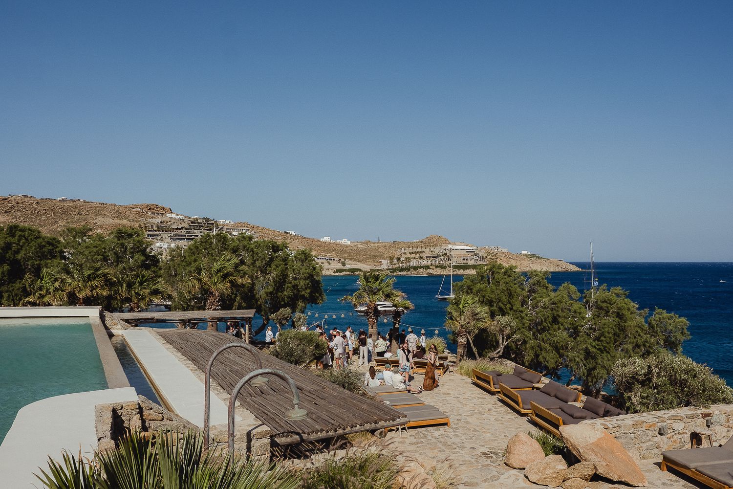 Mediterranean coastal landscape with blue ocean views, rocky cliffs, and beachfront resorts under bright sunny skies.