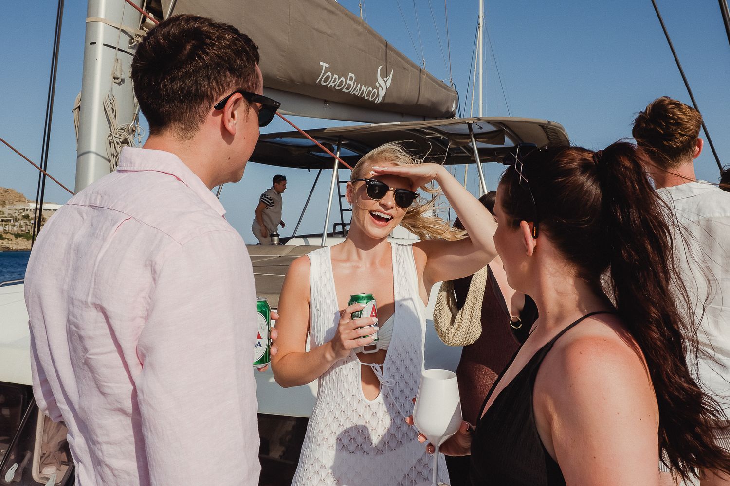 Couple cuddling and celebrating on a boat deck with ocean and coastline views in the background.