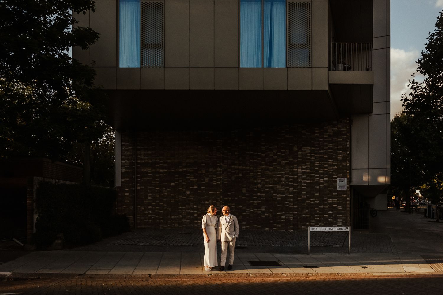 Two people stand together at dusk outside a modern building with stone and glass architectural elements.