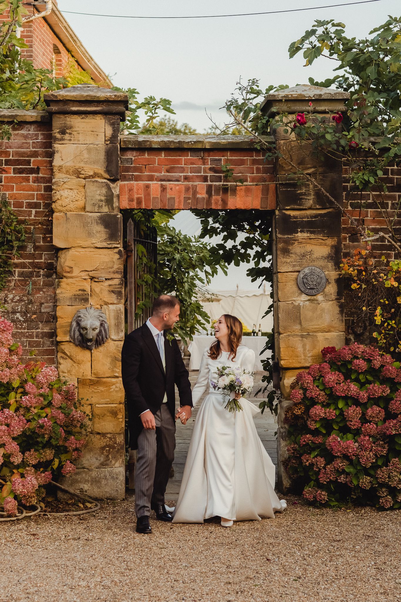 Romantic wedding couple poses against stone garden wall with blooming pink roses in sequence of candid moments.