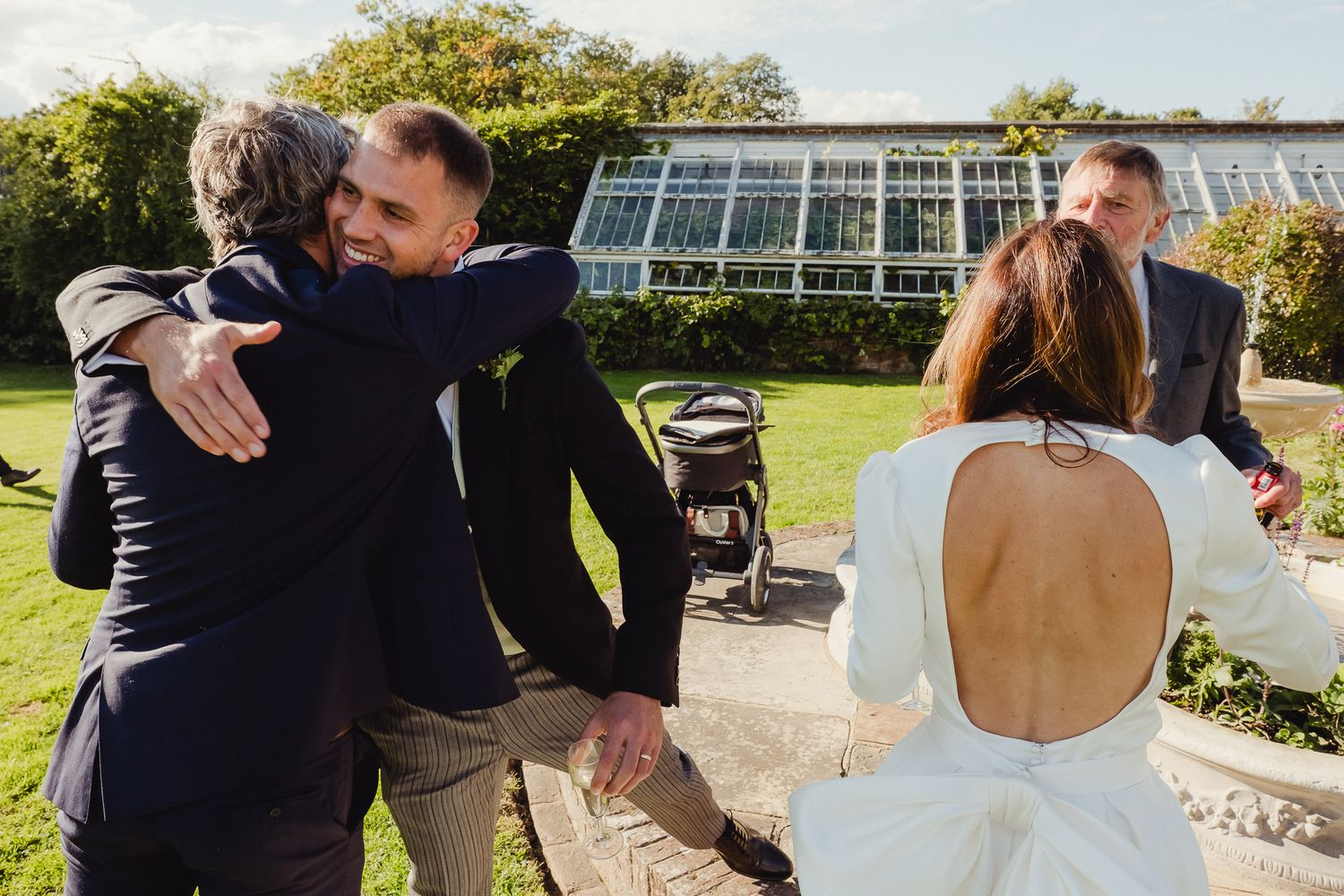 Tender moments shared between couples during an outdoor wedding celebration with garden and greenhouse backdrops.