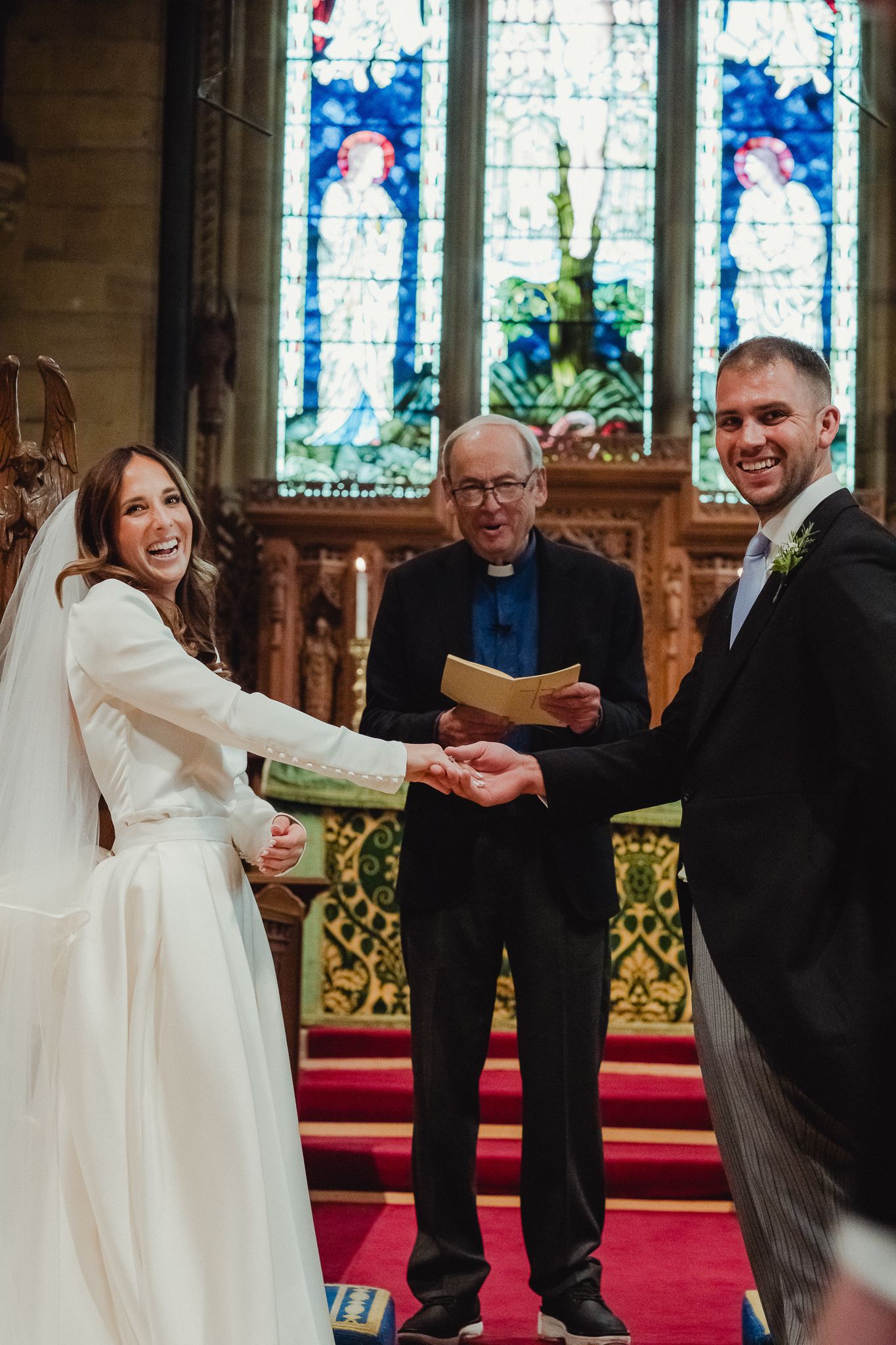 A joyful wedding ceremony unfolds at the altar of a beautiful church with stained glass windows in the background.