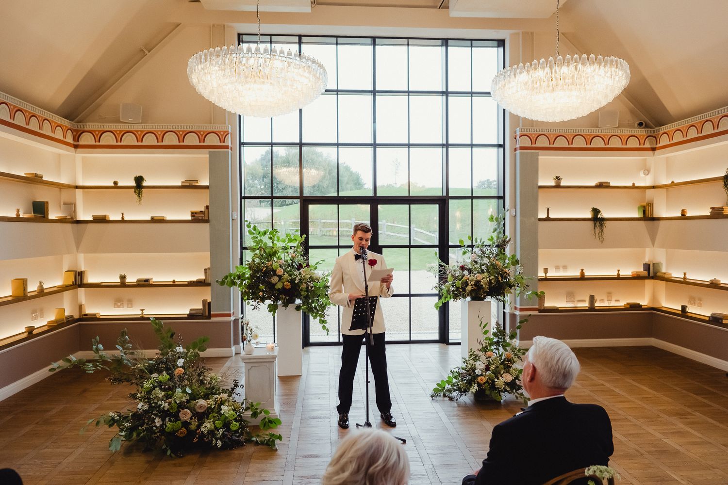 A bright interior space with large windows, floating shelves, and floral arrangements in a modern design setting.