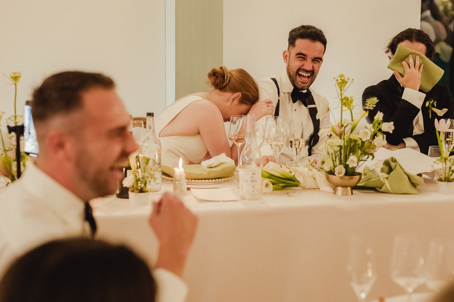 Wedding reception guests seated at long tables decorated with yellow floral centerpieces in an elegant white venue.