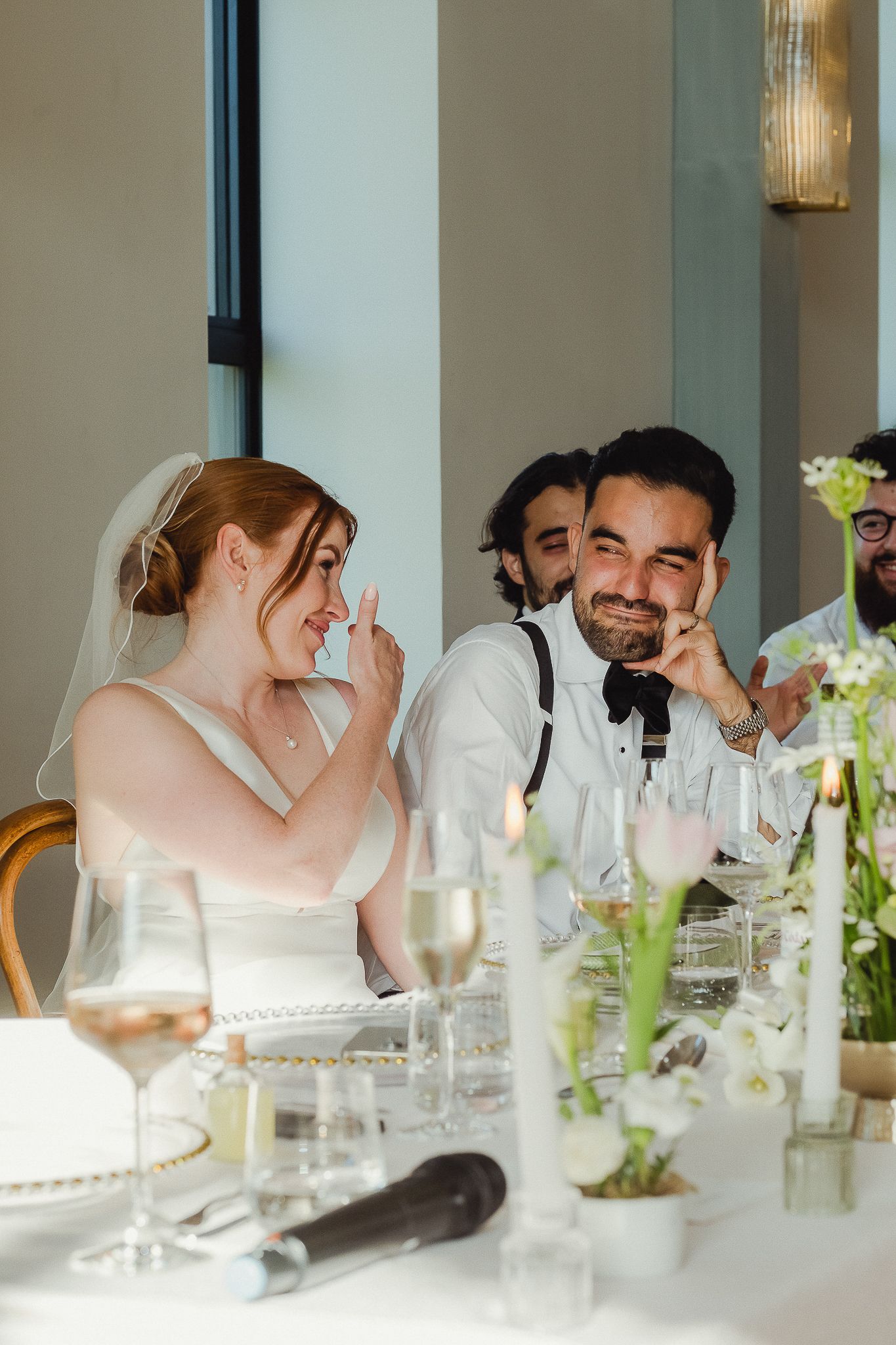 Wedding guests share laughter and conversation at an elegant white-tablecloth reception dinner.