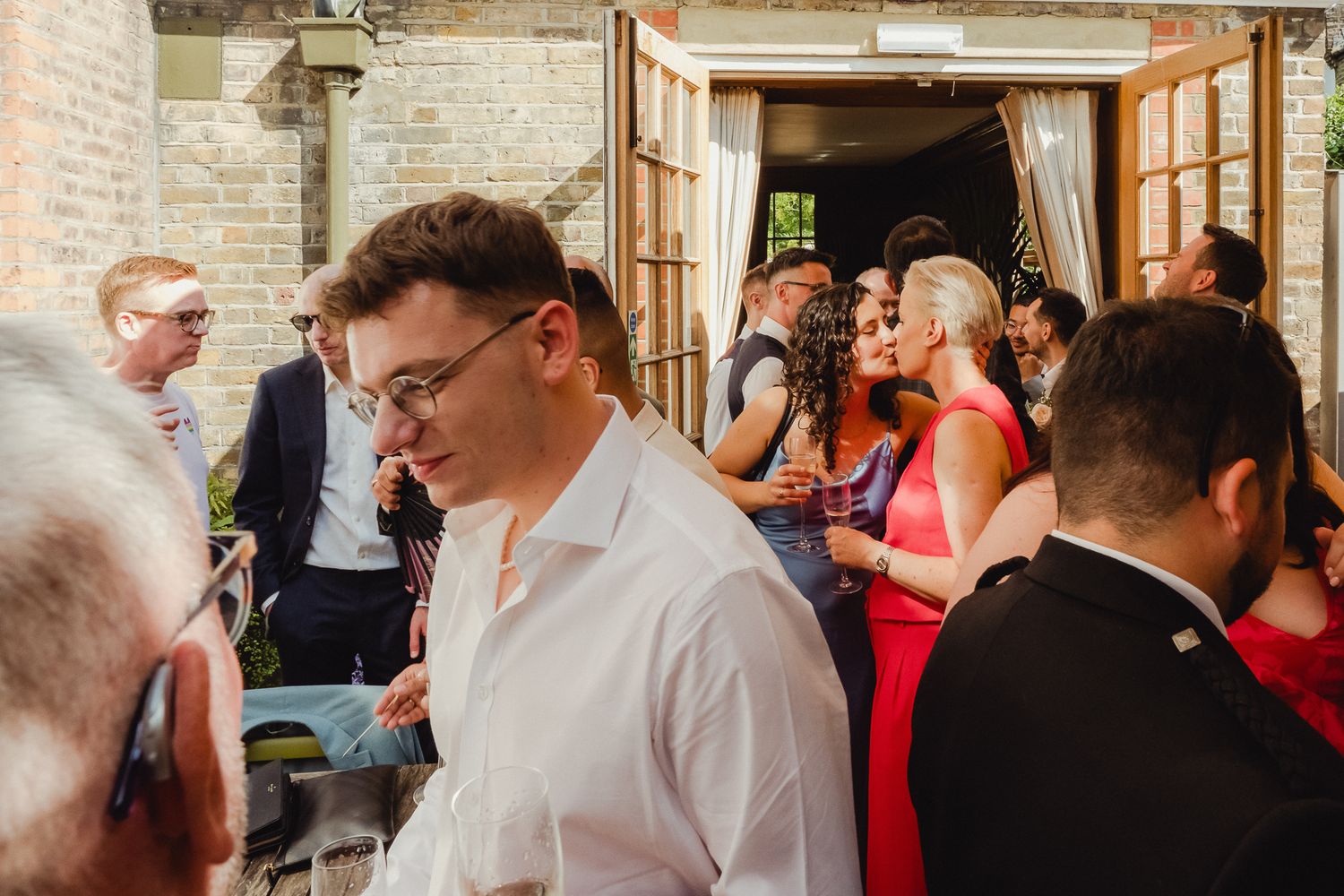 Wedding guests gathered at a reception venue with stone walls and french doors, socializing in formal attire.