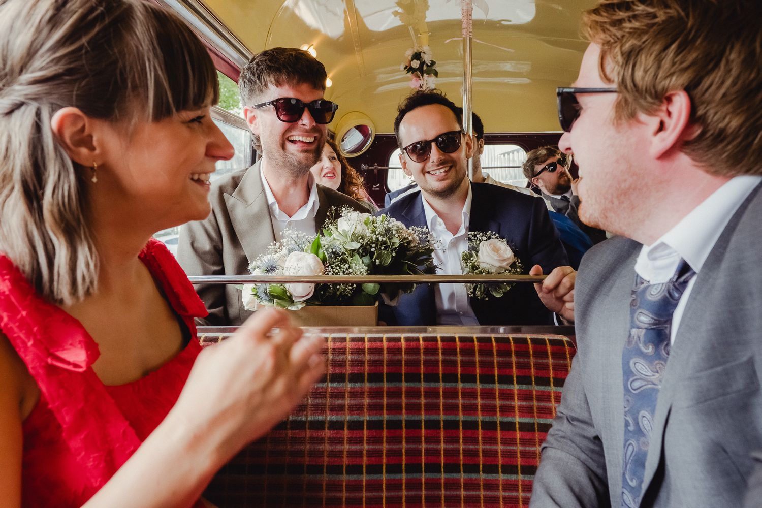 A group of people enjoying drinks and conversation at a wedding reception with red checkered tablecloths.