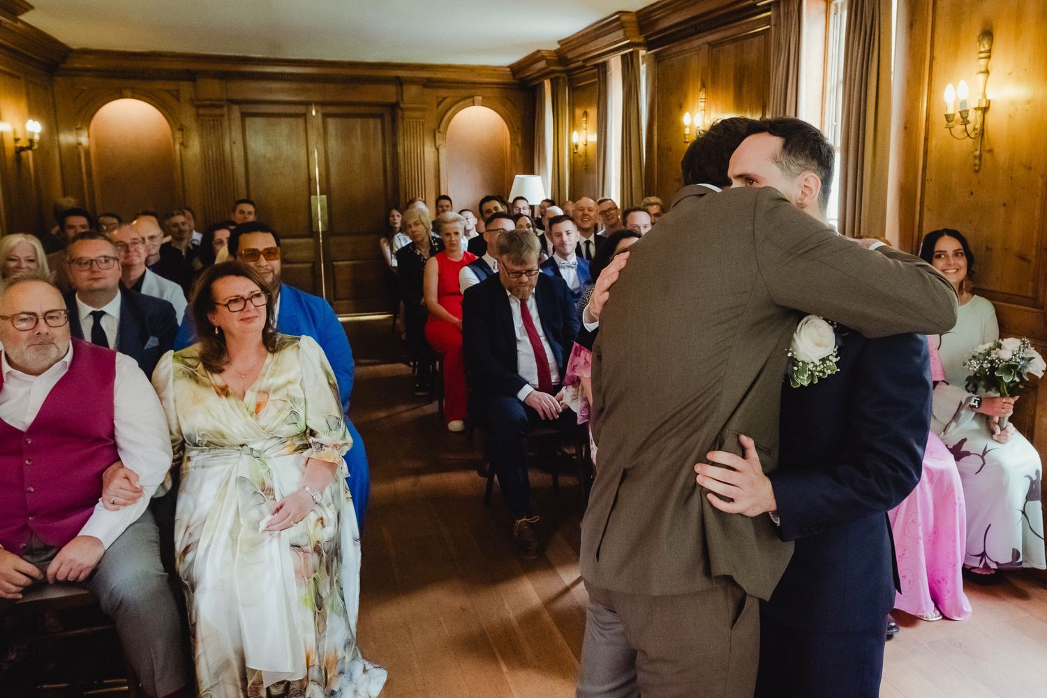 Emotional wedding ceremony moment in an elegant wood-paneled room with guests seated in rows watching the celebration.