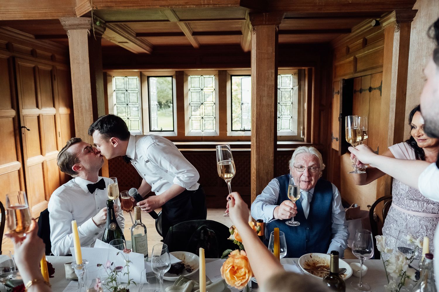 Wedding guests raising champagne glasses in a toast at an elegant wood-paneled reception venue.