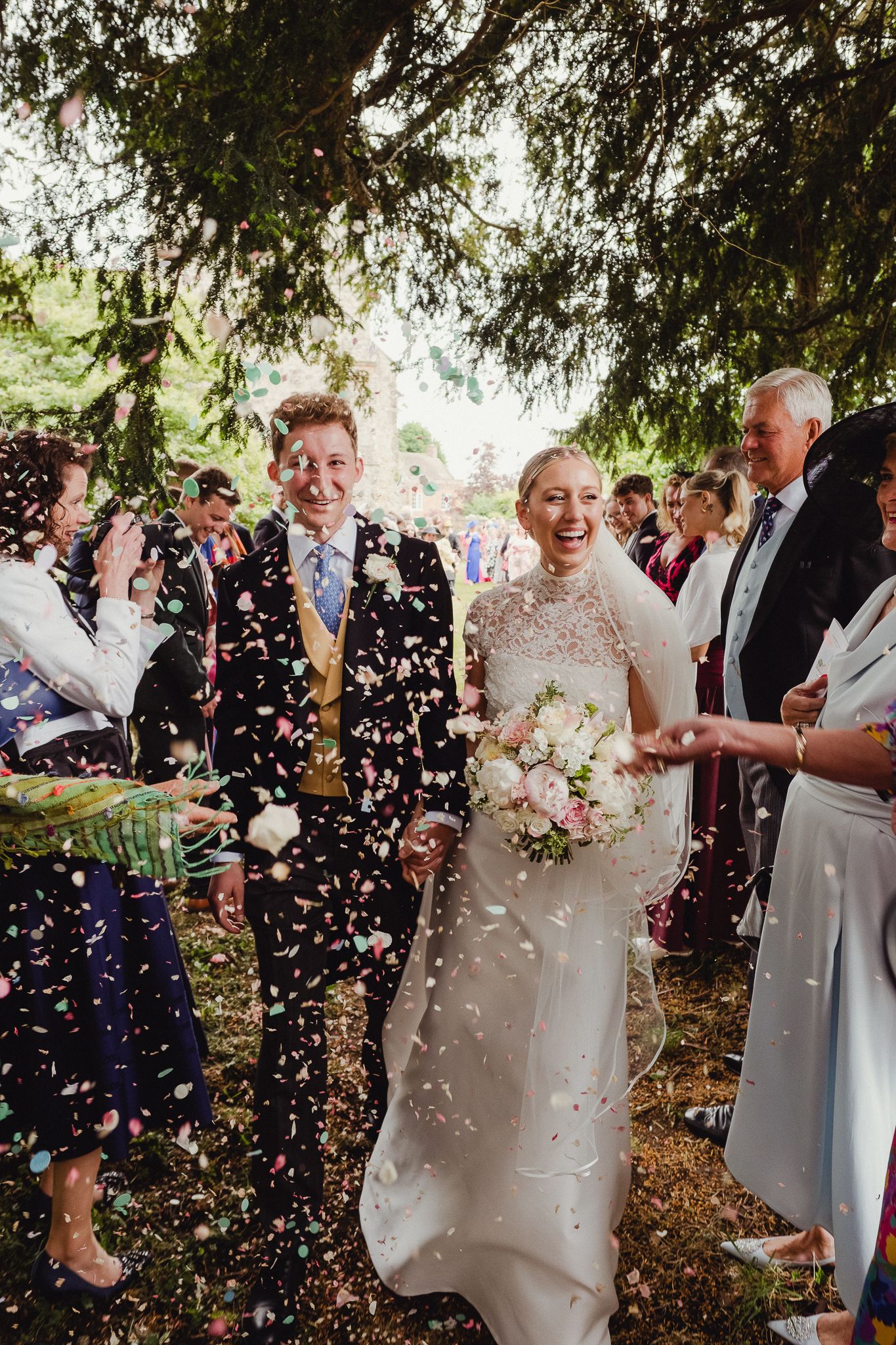A joyous outdoor wedding celebration with confetti being showered over a couple in a natural woodland setting.