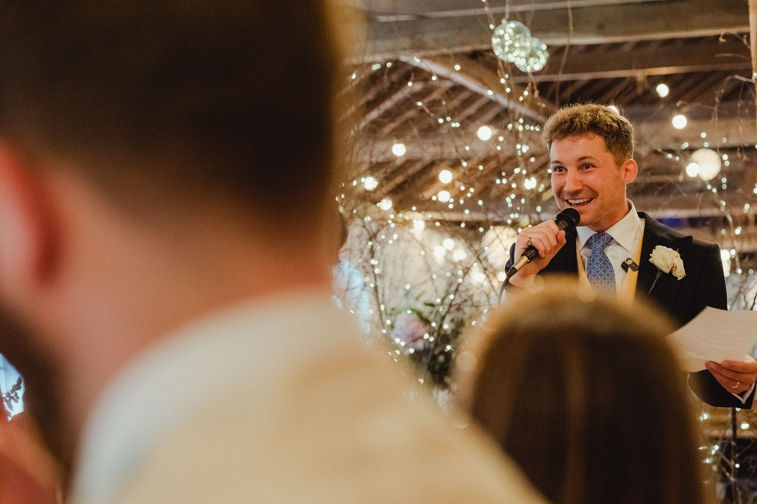 A group of wedding guests laugh and socialize together in a dimly lit reception venue with decorative lights.