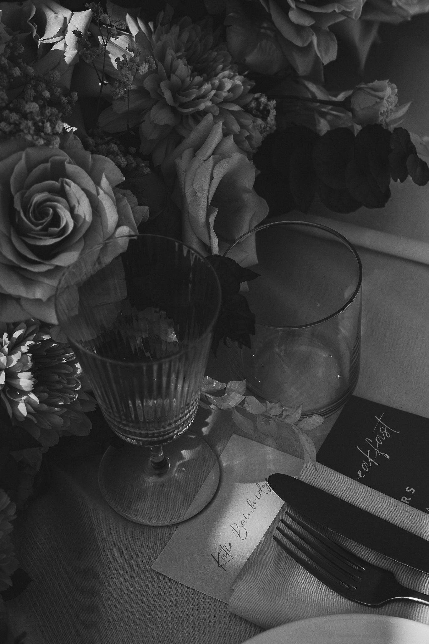 Dark moody grayscale shot of floral arrangements with roses and vases on a table with dramatic lighting and shadows.