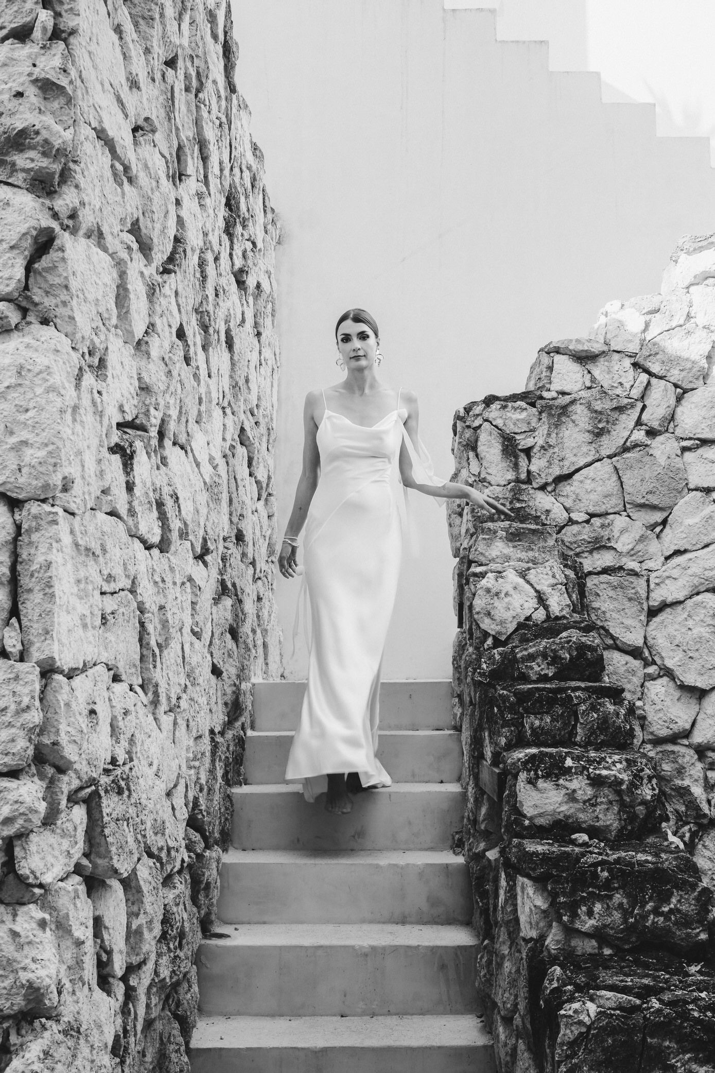 A sequence of black and white photos showing a person in a white dress ascending stone steps against a rustic wall.