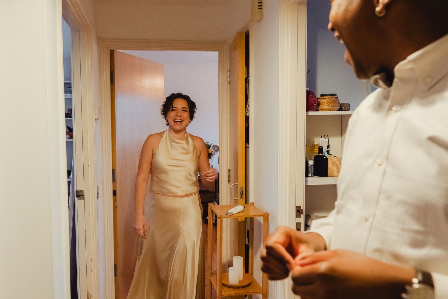 A candid moment in a hallway with someone in a cream-colored dress holding a glass while another person stands nearby.