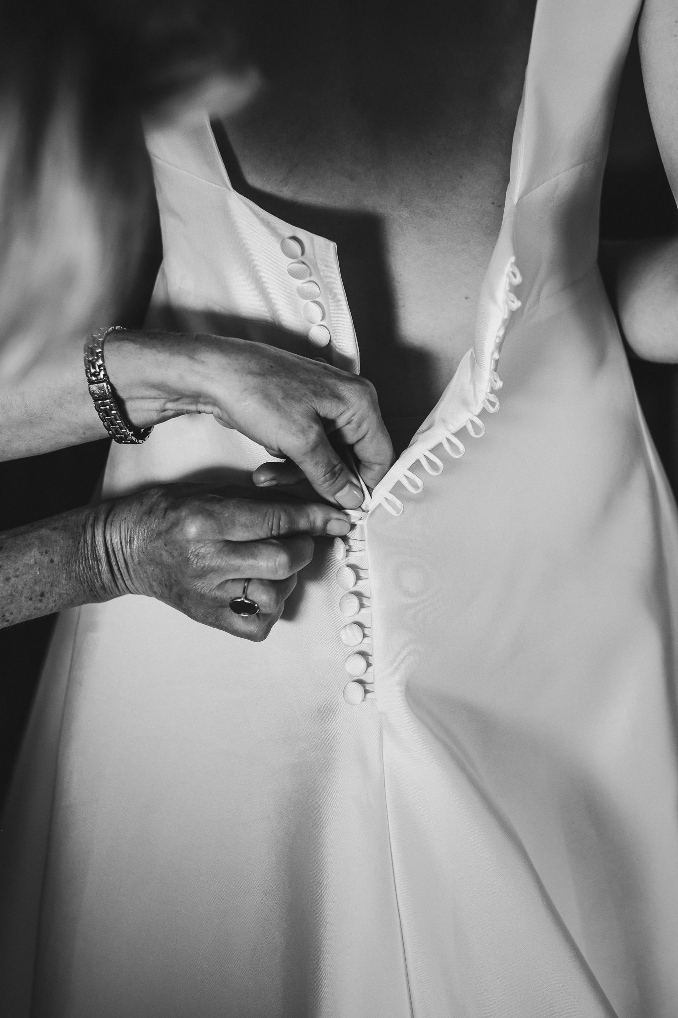 Close-up black and white detail of hands buttoning up wedding dress.