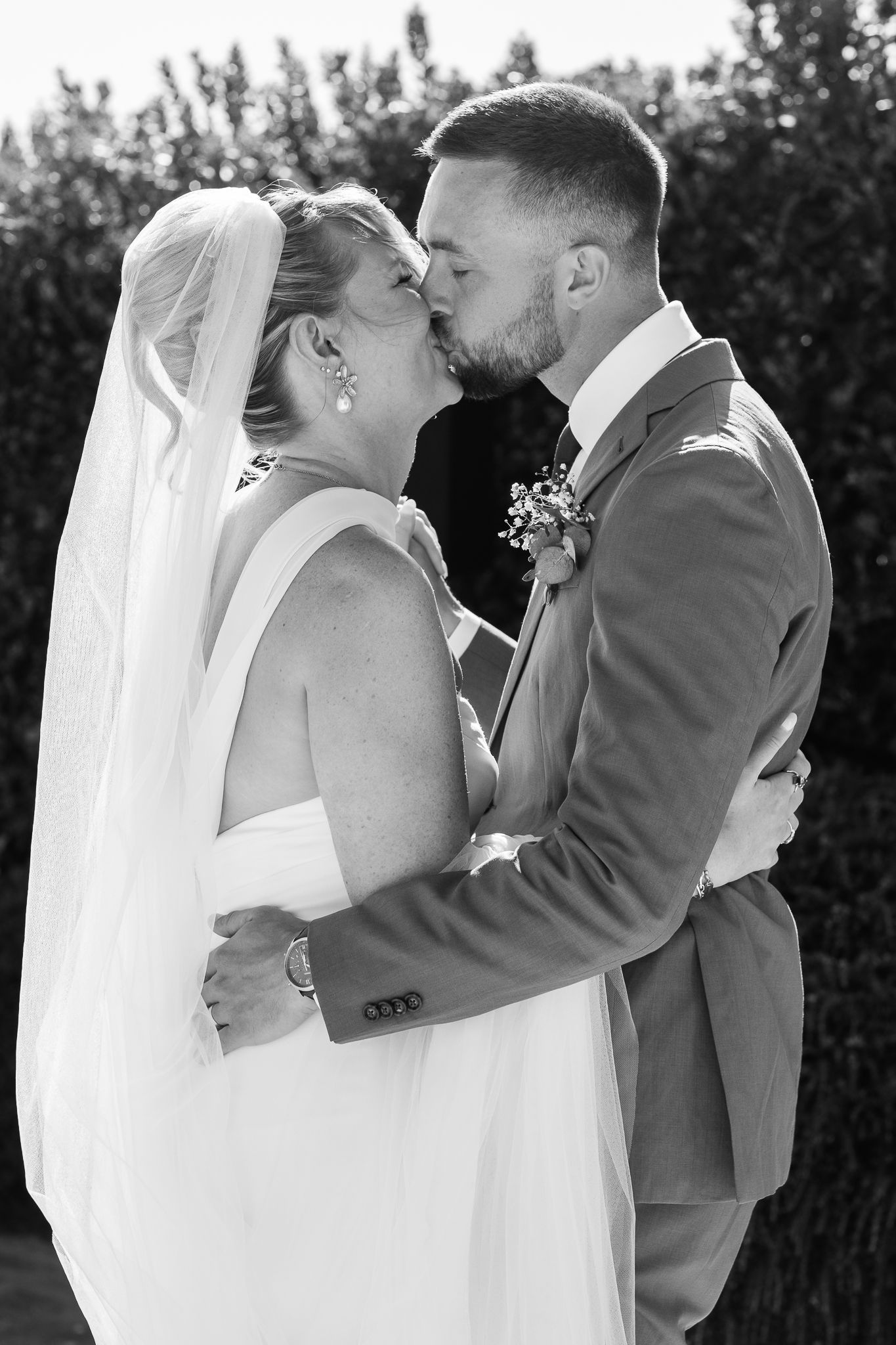 Black and white photo of a bride and groom sharing a kiss outdoors on their wedding day.
