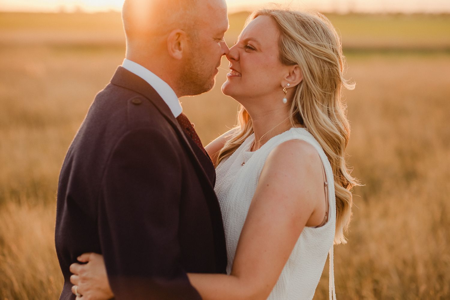 A couple shares an intimate kiss in a golden wheat field at sunset, creating a romantic silhouette.
