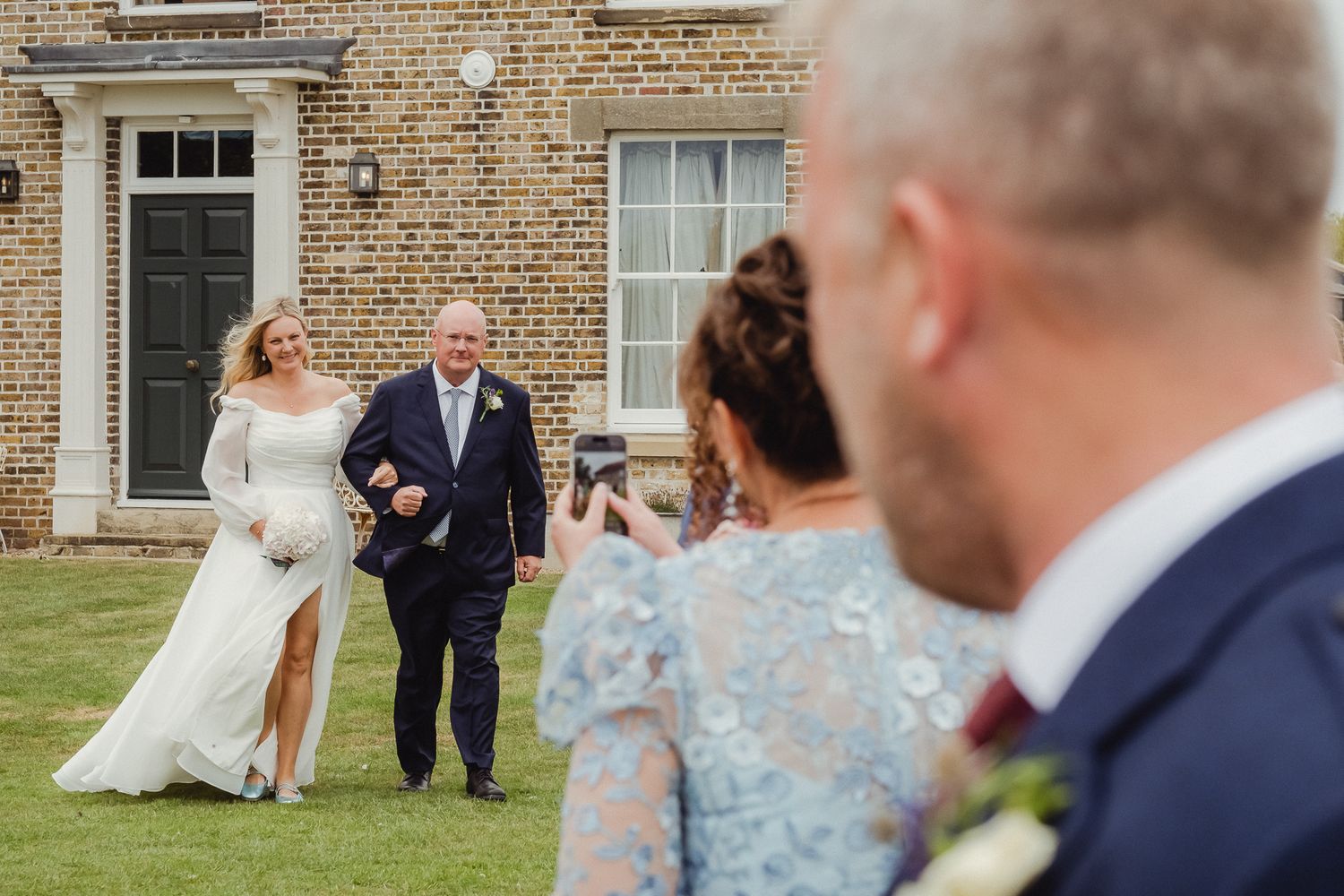 Wedding guests capture a special moment on a lawn in front of a classic brick building.
