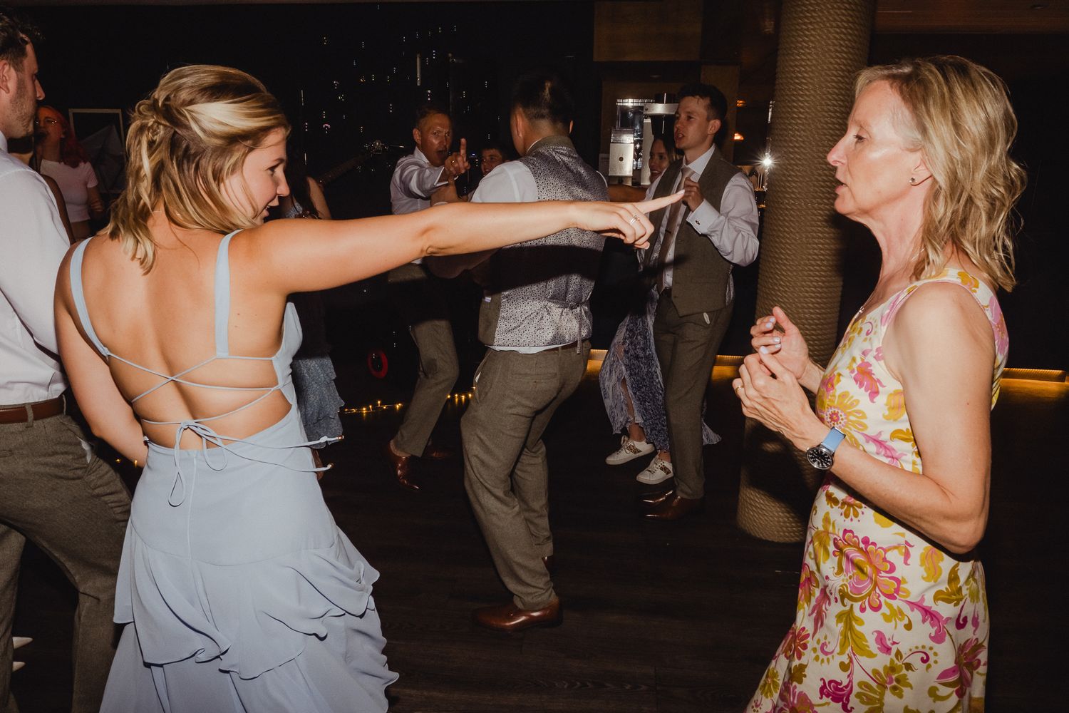 Wedding guests dancing and celebrating on a dark dance floor with bubbles floating through the air.