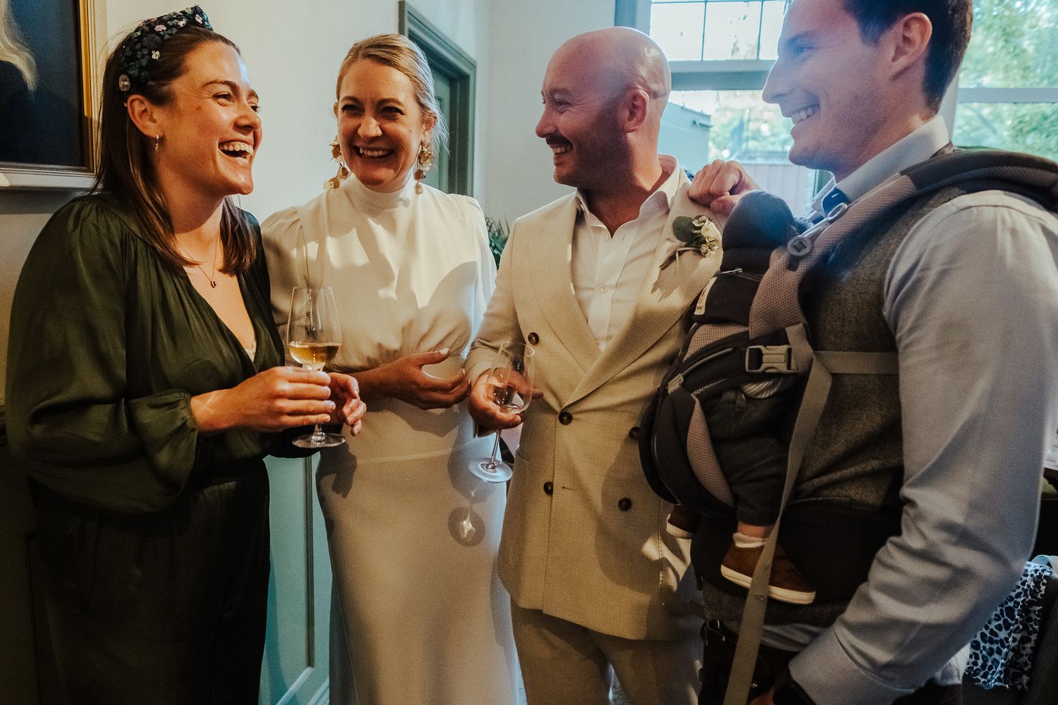 A group of people sharing laughter and conversation in an indoor social setting while enjoying drinks and good company.