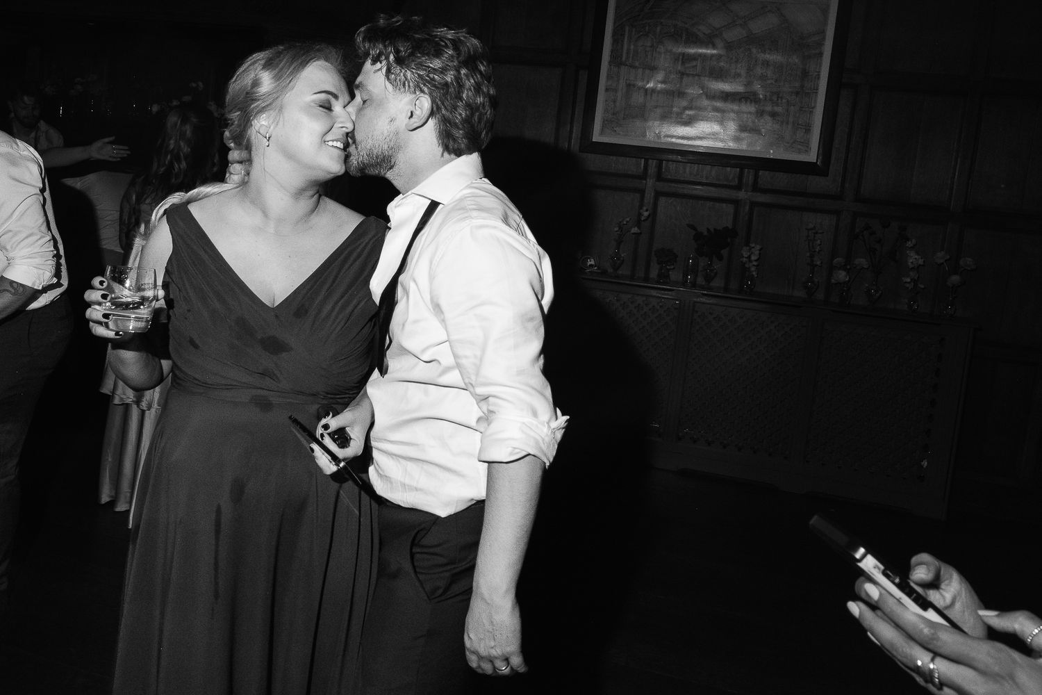Black and white photo of a couple sharing a kiss at a wedding reception party.