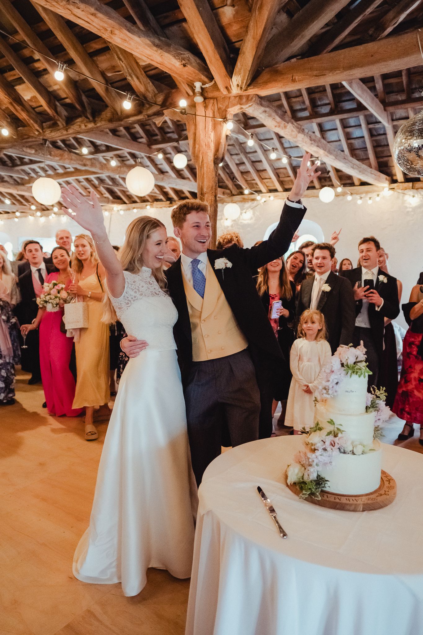 A celebration inside a rustic barn venue with exposed wooden beams and glowing lights during a wedding reception.