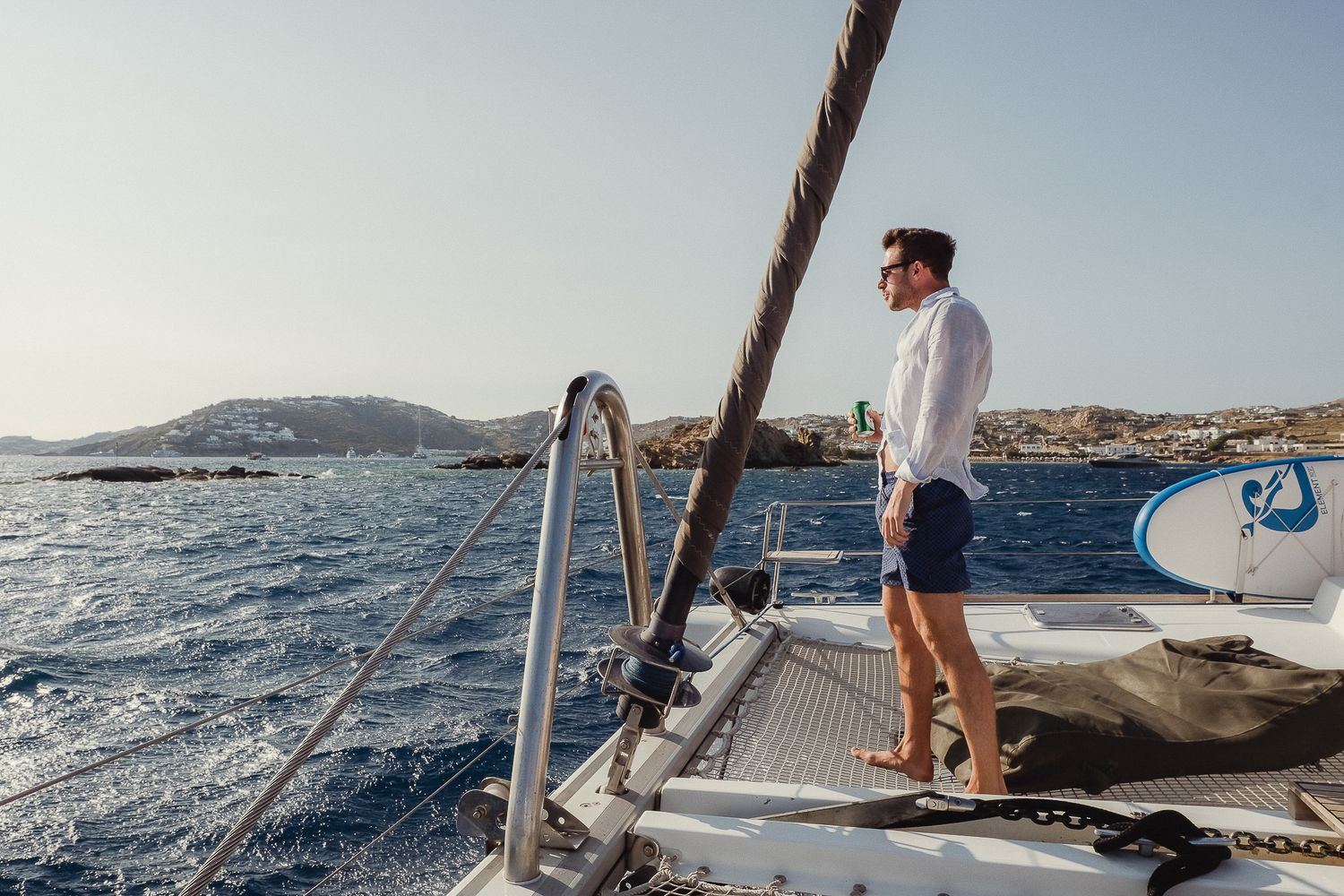A sailing yacht cruises through blue Mediterranean waters on a sunny day while passengers enjoy the deck.