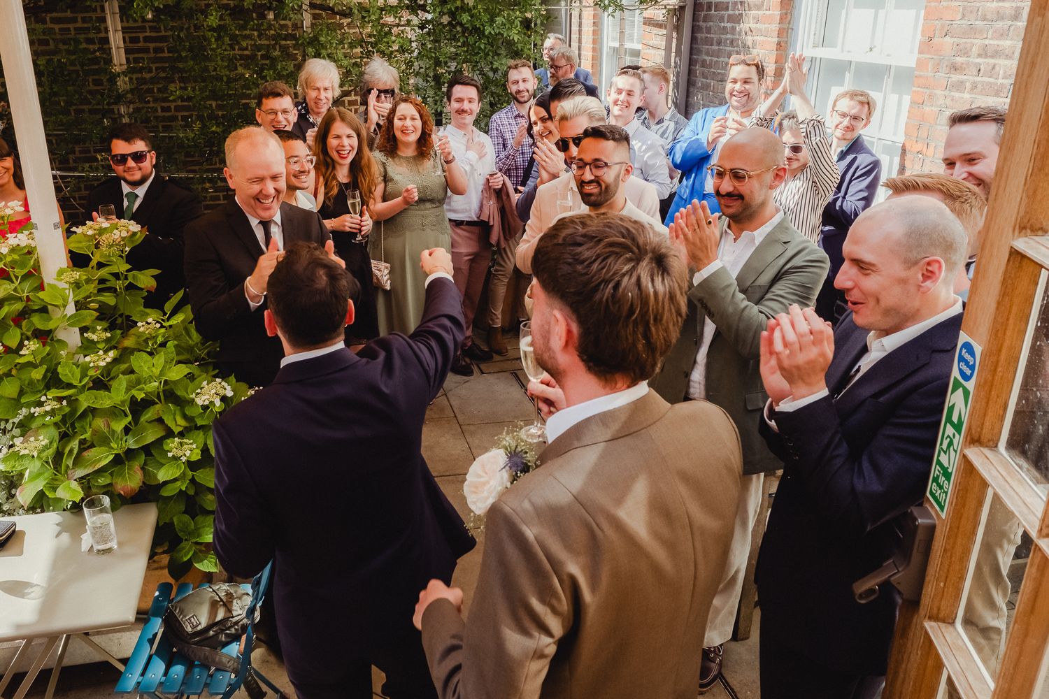 Wedding guests gathered in a reception venue with brick walls and natural lighting during a celebration.