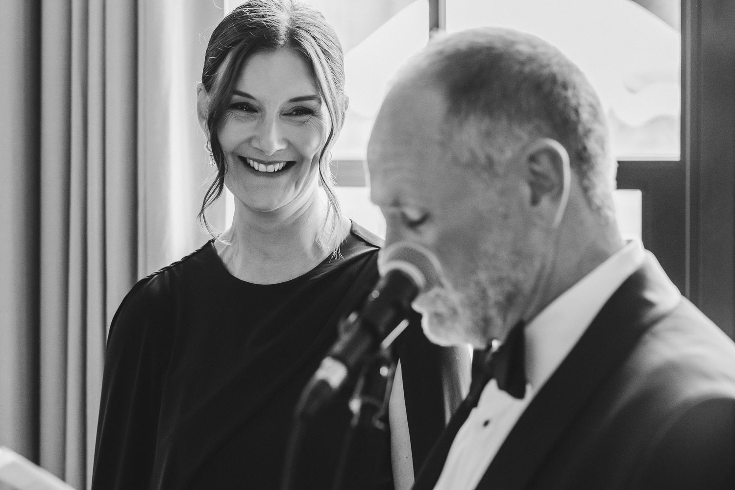 People in formal attire share a candid moment of laughter during a black and white event.