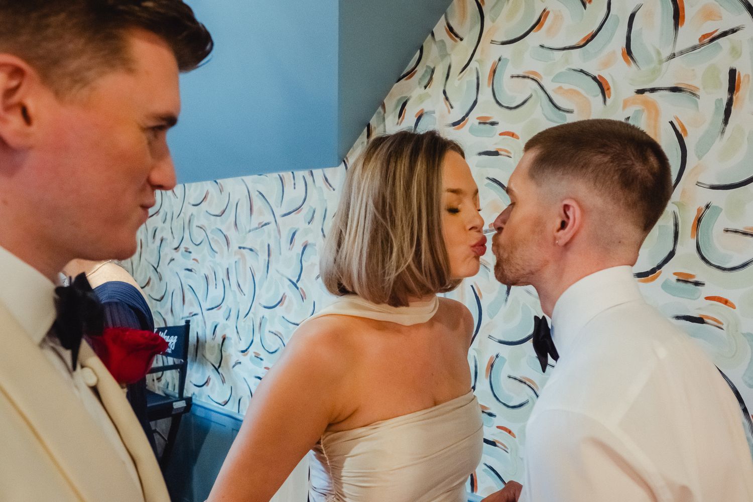 A couple shares an intimate moment at their wedding ceremony against a decorative patterned wall.