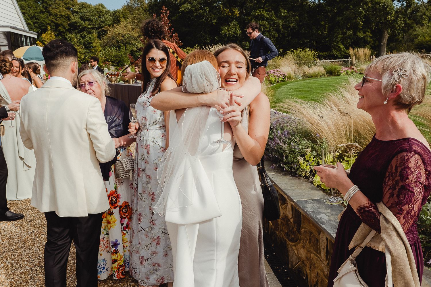Wedding guests celebrate with confetti at an outdoor garden reception on a sunny afternoon.