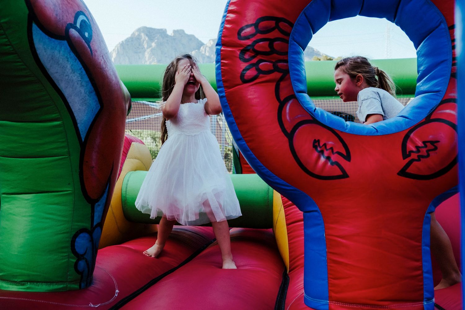 Someone in a white dress jumps on a colorful inflatable bounce house with mountains in the background.