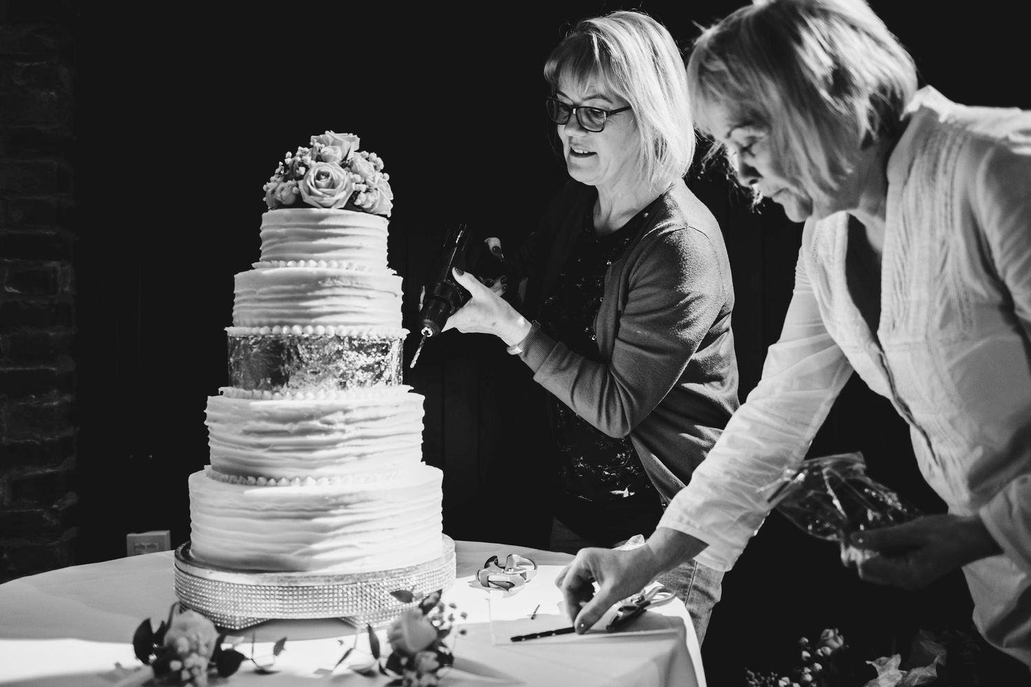 Two guests examine an elegant tiered wedding cake at reception.