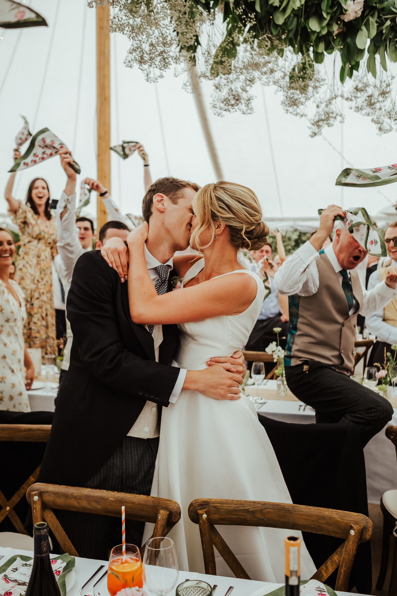 Wedding guests share joyful laughter and embraces during a sunlit outdoor reception celebration.