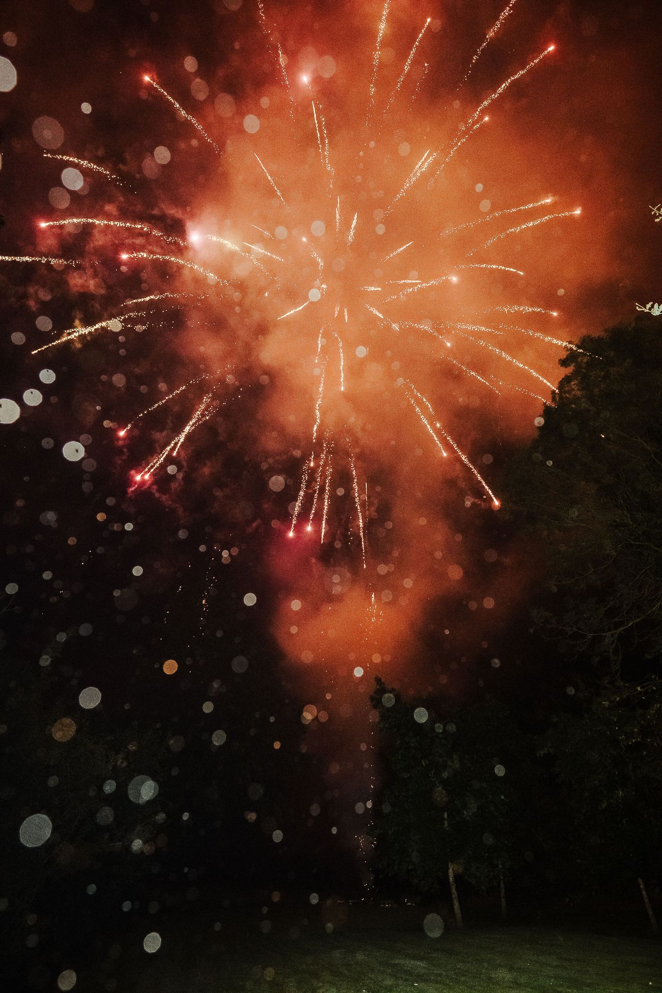Dramatic red and orange fireworks explode in the night sky with bokeh light effects.