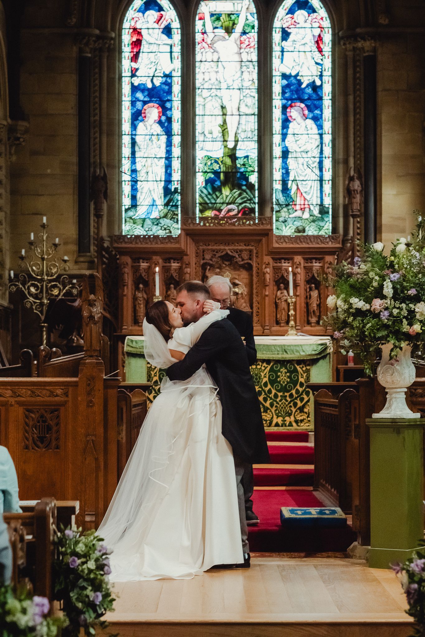 A romantic wedding ceremony takes place inside a beautiful church with stained glass windows and ornate wooden details.