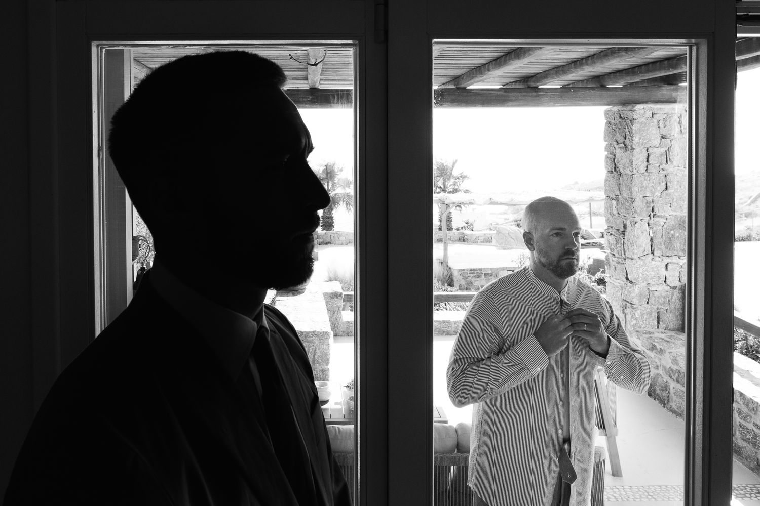 Black and white photo of two men, one silhouetted in foreground, another adjusting tie in doorway.