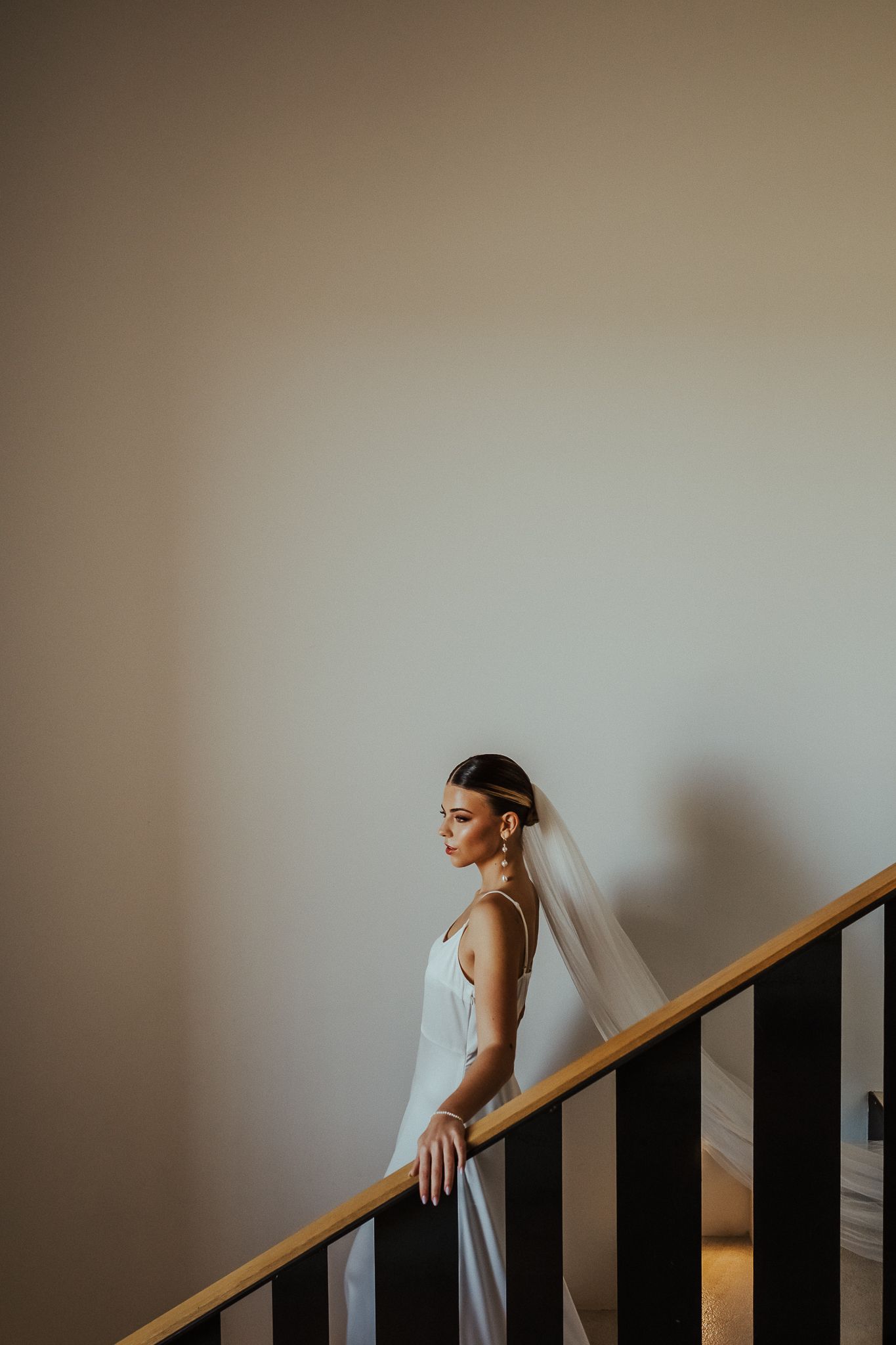 A figure in a white dress stands on a staircase against a neutral wall, creating a minimalist artistic composition.