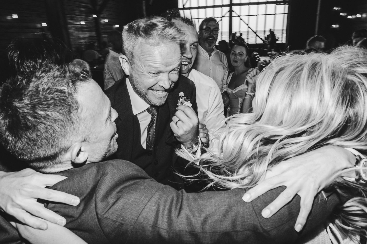 A black and white photograph shows people dancing and embracing at what appears to be a social gathering or party.