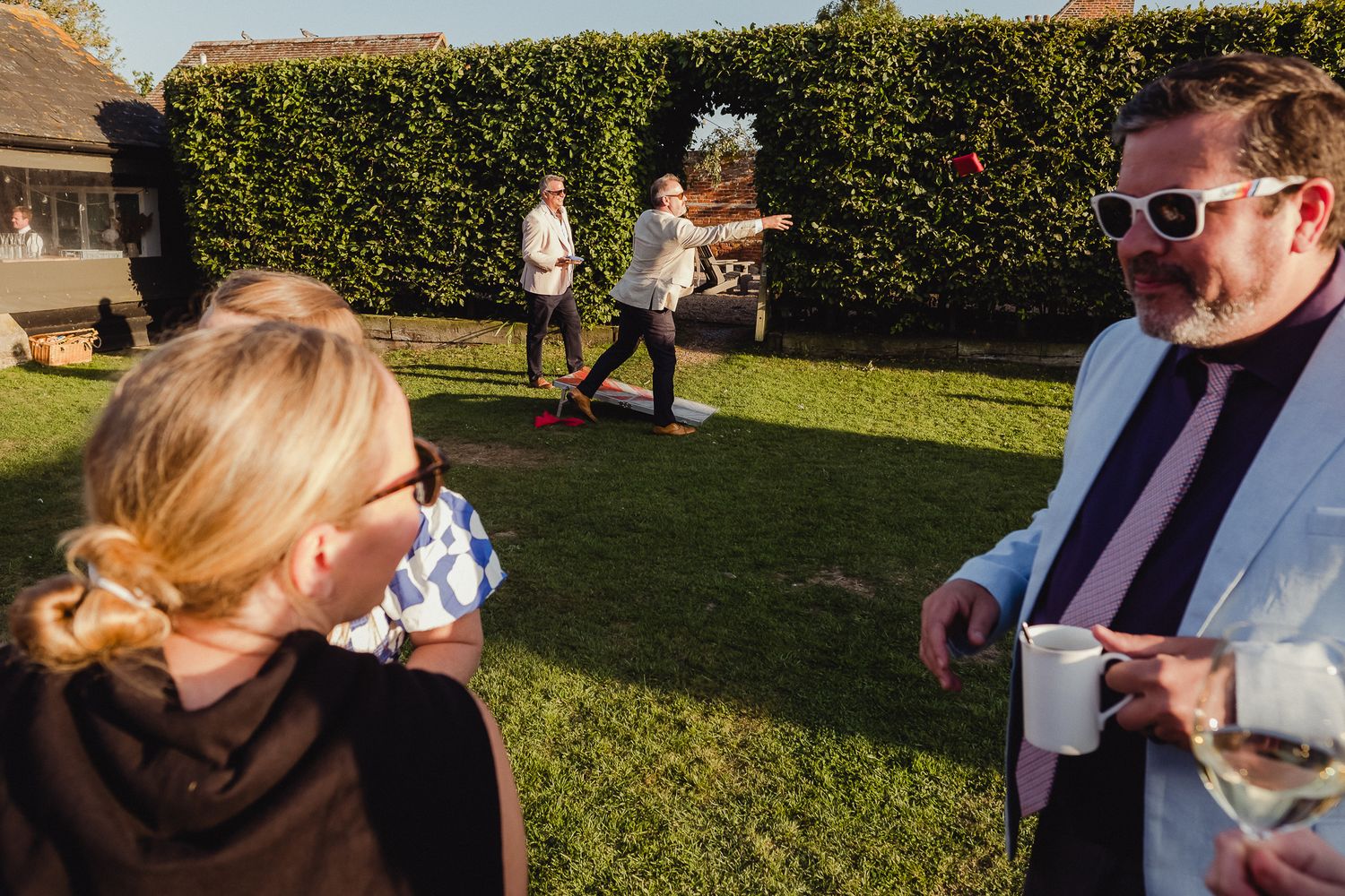 A group of people enjoy an outdoor gathering in a backyard garden setting on a sunny day.