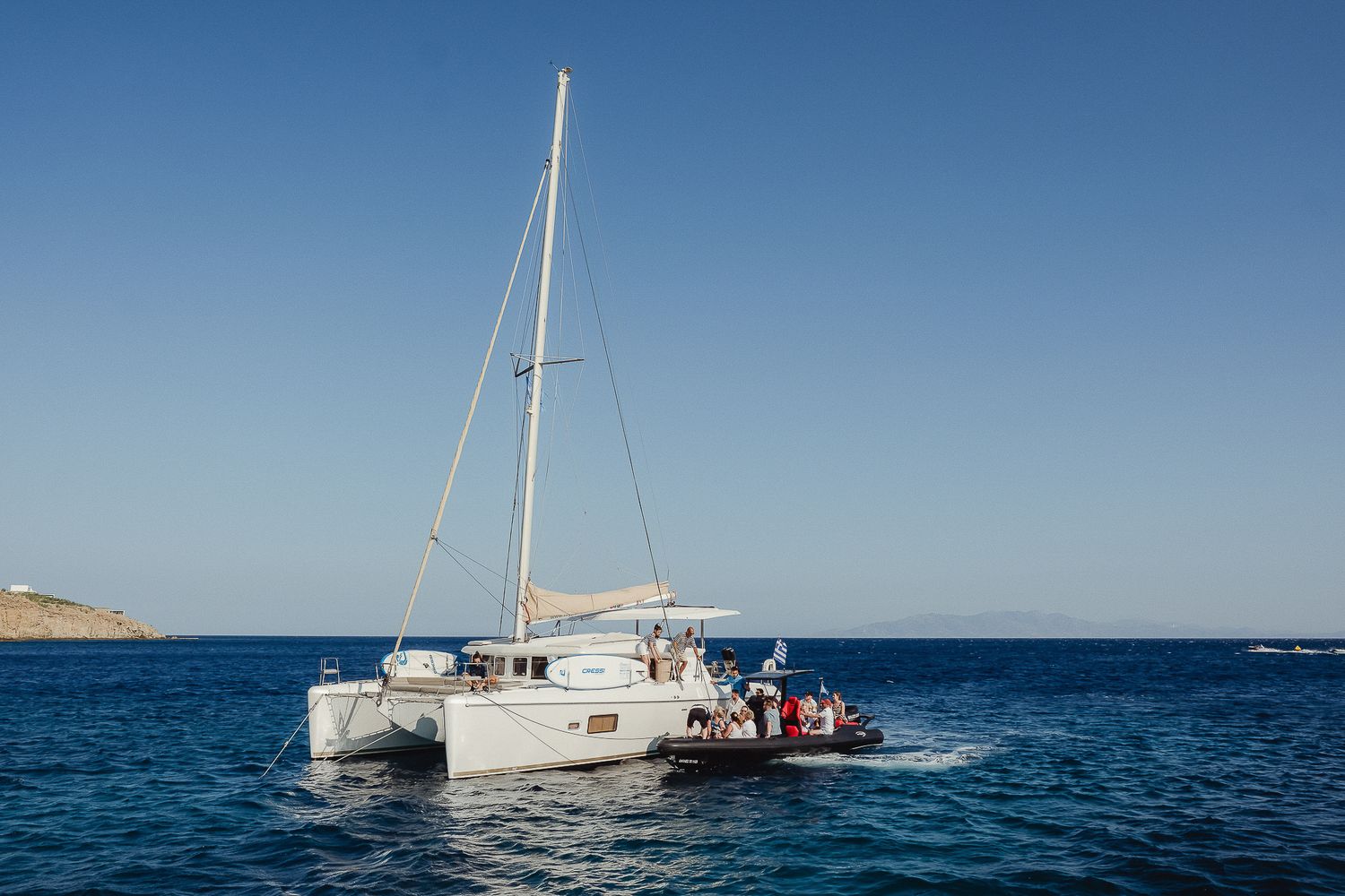White sailboat rests calmly on calm blue ocean waters with clear skies overhead and distant mountains visible.