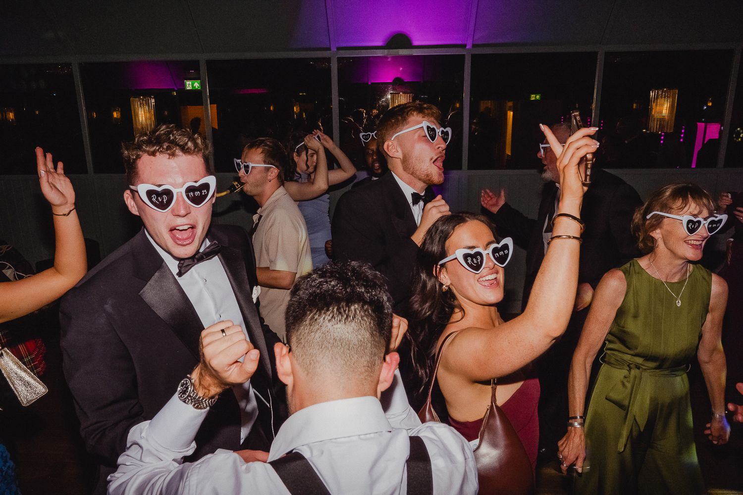 People dancing and celebrating at a dark nightclub with purple lighting and energetic atmosphere.