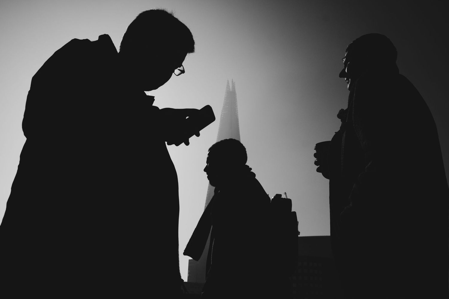 Silhouetted figures stand in a row against a light background creating a dramatic contrast effect.
